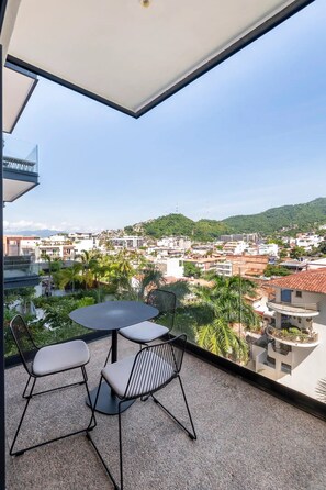 Ein Balkon mit Tisch und Stühlen, mit Blick auf eine Stadtlandschaft mit Gebäuden und Grünflächen.