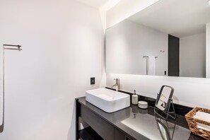 Ein modernes Badezimmer mit einem weißen Waschbecken, einem großen Spiegel und einer schwarzen Arbeitsplatte.