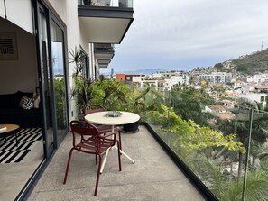 Ein Balkon mit Tisch, Stühlen, einer Couch und Blick auf eine Stadtlandschaft.