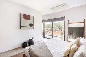 Ein modernes Schlafzimmer mit einem großen Bett, Blick auf die Stadt durch eine Schiebetür, einem Gemälde an der Wand und einem Deckenventilator.