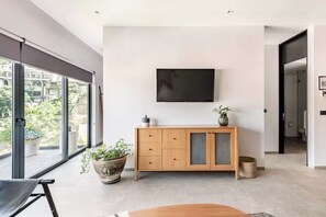 Ein modernes Wohnzimmer mit großem Fenster, einem wandmontierten Flachbildfernseher, einer Holzvitrine und einem Topf mit Pflanze.