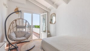 A bedroom with a bed, a hanging chair, a mirror, and a view through a glass door. - Holiday Home “Villa Sol Del Este, Es Castell” with Sea View, Wi-Fi and Air Conditioning (Sol del Este)