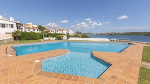 A swimming pool with a tiled deck, surrounded by greenery and a view of the sea. - Holiday Home “Villa Sol Del Este, Es Castell” with Sea View, Wi-Fi and Air Conditioning (Sol del Este)