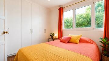 Une chambre à coucher avec un lit, une table de chevet avec une lampe, une fenêtre avec des rideaux et une porte avec une poignée.