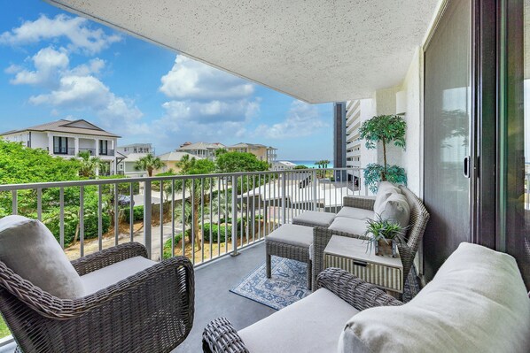 A balcony with wicker furniture, a view of the ocean, and neighboring buildings. - Mainsail 322 - Beachfront Condo, Free Bch Svc, Pool, Hot Tub, Tennis! (Miramar Beach)