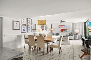 A modern living room with a dining area, white walls, and a large window. - Mainsail 322 - Beachfront Condo, Free Bch Svc, Pool, Hot Tub, Tennis! (Miramar Beach)