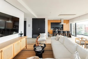Ein modernes Wohnzimmer mit großem Fernseher, einer Couch, einem Couchtisch und einem Essbereich mit Stühlen.