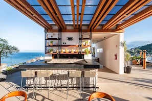 Eine Dachterrasse mit Blick auf das Meer, Holzbalken und einer Bar.