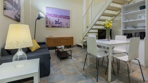A living area with a sofa, a coffee table, a lamp, a painting, a dining table with chairs, a bookshelf, and a staircase. - Loft San Carlo by Wonderful Italy (Turin)