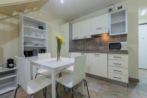 Una cocina moderna con armarios blancos, una mesa de comedor con sillas, una cafetera y un microondas.