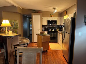 Et køkken med mikrobølgeovn, komfur, ovn og køleskab. Der er et spiseområde med et bord og stole. En lampe står på bordpladen.