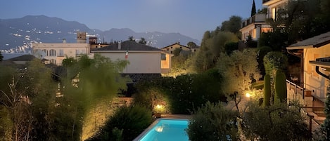 A pool surrounded by greenery and buildings, with a mountain backdrop and a visible moon.