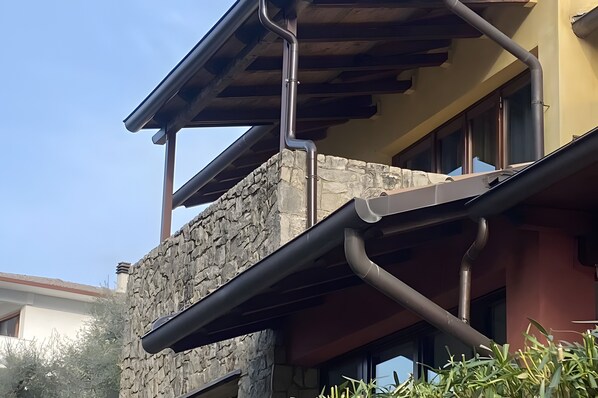 Un edificio con facciata in pietra, un balcone con ringhiera in metallo e una struttura del tetto in legno.