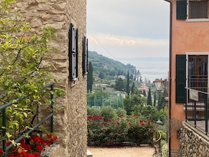 Un edificio de piedra con un balcón y vistas a la costa, con flores rojas en primer plano.