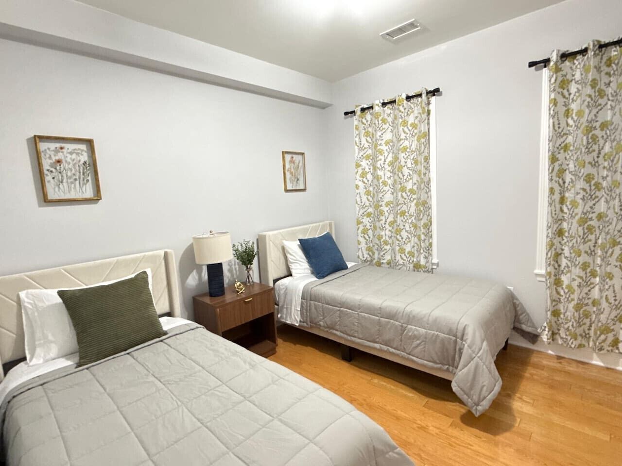 Une chambre avec deux lits, une table de chevet, une lampe et des rideaux à motifs floraux.