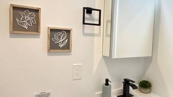 A bathroom with a toilet, sink, and mirror. There are two framed floral decorations on the wall.