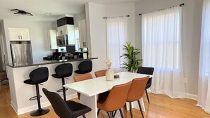 Uma cozinha moderna com armários brancos, uma ilha central e uma área de jantar com mesa e cadeiras brancas.