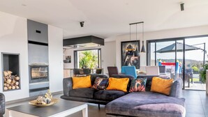 A modern living room with a sectional sofa, a fireplace, and a large window offering a view of the outdoors. - Villa with jacuzzi, 5 bedrooms - ideal for families (Inzinzac-Lochrist)