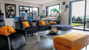 A modern living room with a dark sofa, a coffee table, and a large window offering a view of the outdoors. - Villa with jacuzzi, 5 bedrooms - ideal for families (Inzinzac-Lochrist)