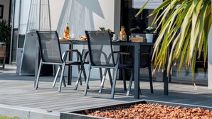 A modern outdoor dining area with a table and chairs, a fire pit, and a view of a building with a balcony. - Villa with jacuzzi, 5 bedrooms - ideal for families (Inzinzac-Lochrist)