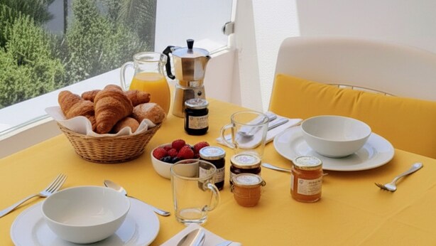 Une table de petit-déjeuner avec des croissants, des fruits rouges, du miel et du café, le tout disposé devant un paysage marin magnifique.