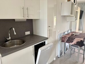 A compact kitchen with a stainless steel sink, a dishwasher, and a dining area with a table and chairs. - Apartment Near the Beach with Ocean View, Just Steps Away (Costa Adeje)