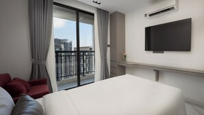A modern hotel room with a large bed, a flat-screen TV, a balcony with curtains, and a city view. - Pinnacle Moments Residence (Phnom Penh)