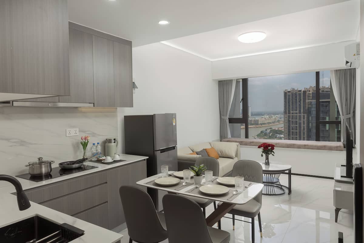 A modern kitchen with a dining area, a sofa, and a view of a cityscape.