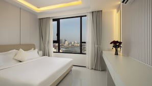 A modern hotel bedroom with a large bed, a city view, and a bedside table with a vase of flowers. - Pinnacle Moments Residence (Phnom Penh)