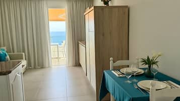 A dining area with a table set for two, a view to the sea, and a balcony with curtains.