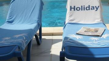 Twee lounge stoelen bij een zwembad, met een 'Holiday' handdoek op één van de stoelen.