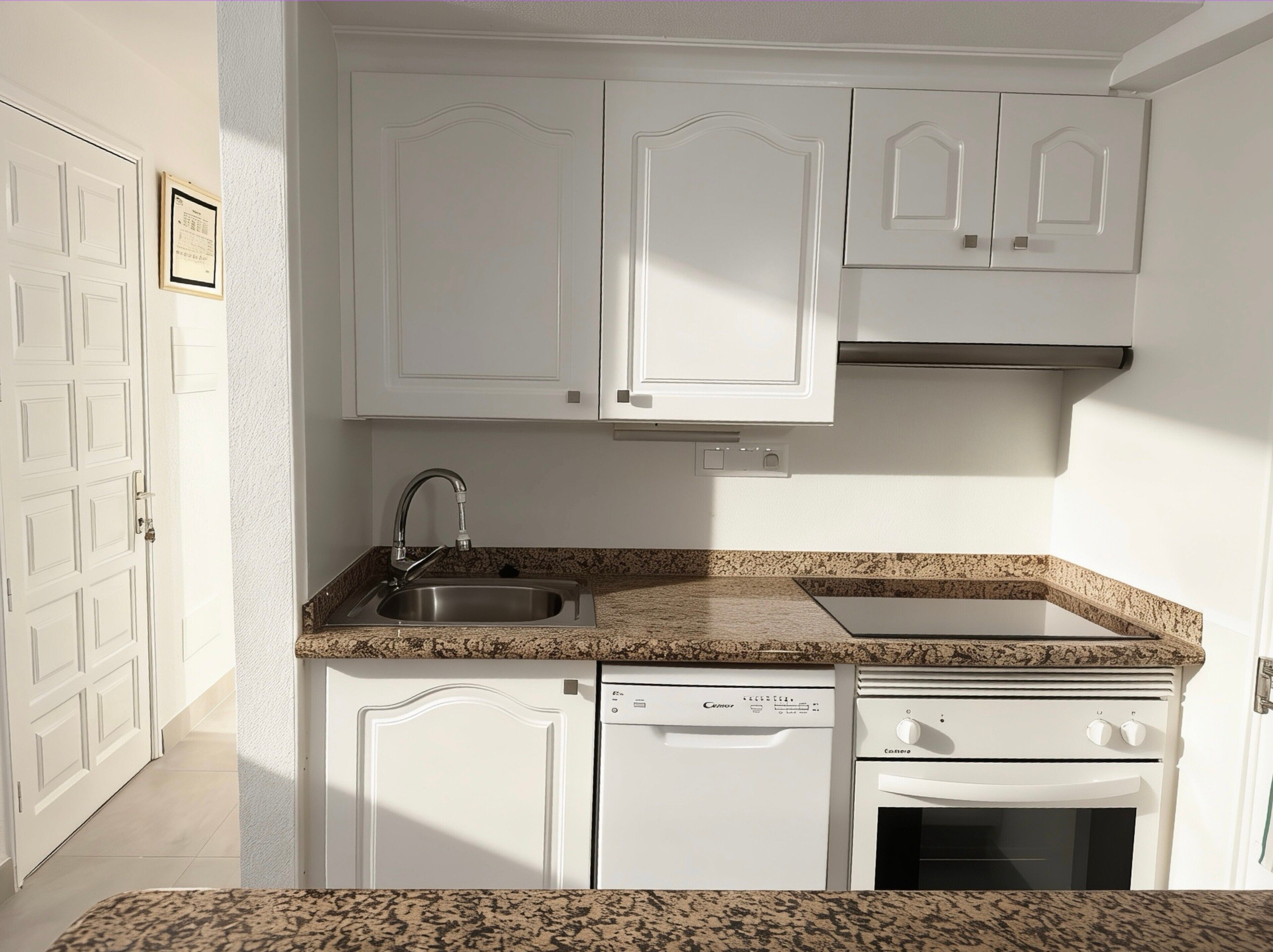A compact kitchen with white cabinetry, a stainless steel sink, a dishwasher, and an oven.