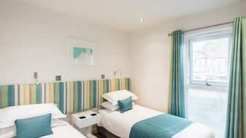 A hotel room with two beds, a striped headboard, a window with curtains, and a small bedside table with a lamp.