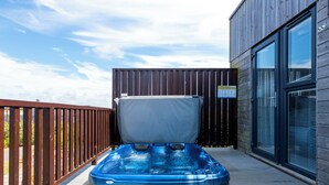 A hot tub on a wooden deck with a wooden fence and a building with large windows. - Barbara (Redruth)
