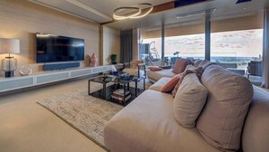 Ett modernt vardagsrum med en stor platt-TV, en soffa, ett soffbord och utsikt över staden.