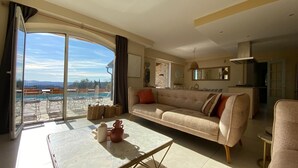 Ein geräumiges Wohnzimmer mit großem Fenster, einer Couch, einem Couchtisch und Blick auf einen Swimmingpool.