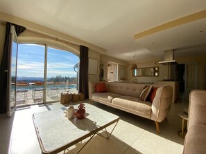 A spacious living room with a large window, a sofa, a coffee table, and a view of a swimming pool. - "Moo Graugh Hoo" Villa (Châteauneuf-Grasse)