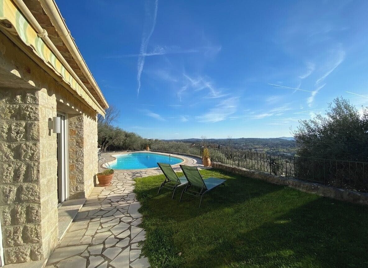 A stone building with a pool, green lawn, and a view of the countryside.