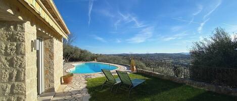 A stone building with a pool, green lawn, and a view of the countryside.