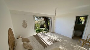 Ein Schlafzimmer mit einem Bett, einem Sessel, einer Wanddekoration aus Makramee und Blick ins Freie.