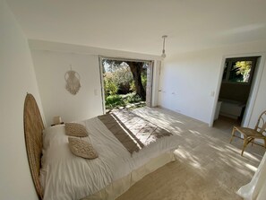 A bedroom with a bed, a chair, a macrame wall hanging, and a view of the outdoors. - "Moo Graugh Hoo" Villa (Châteauneuf-Grasse)