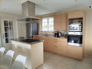 A modern kitchen with a central island, stainless steel appliances, and wooden cabinetry. - "Moo Graugh Hoo" Villa (Châteauneuf-Grasse)