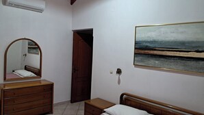 Ein Schlafzimmer mit Bett, Kommode, Spiegel, Tür und einem Bild von einer Strandlandschaft.