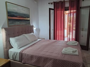Een slaapkamer met een bed, een hoofdbord, een schilderij aan de muur en een deur voorzien van gordijnen.