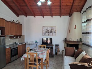A kitchen with wooden cabinets, a dining table with chairs, a TV, and a fireplace. - Krista House is a unique family home in a perfect location for a beach holiday. (Agios Giordios)