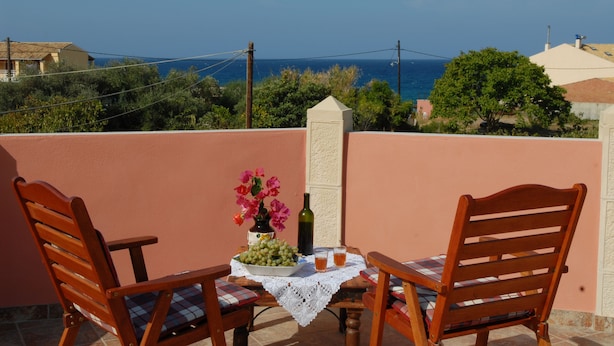 Eine Terrasse mit zwei Holzstühlen, einem Tisch mit Spitzenleinentuch, einer Flasche und einer Schale mit Trauben.