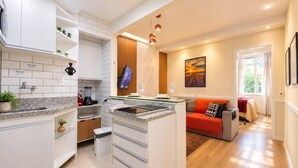 A modern kitchen with a built-in island, a dining area with a red sofa, and a large window providing natural light. - Comfort in Ipanema Near the Beach (Rio de Janeiro)