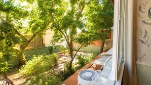 A room with a view of a garden, a window with a curtain, and a fan on the windowsill. - Comfort in Ipanema Near the Beach (Rio de Janeiro)