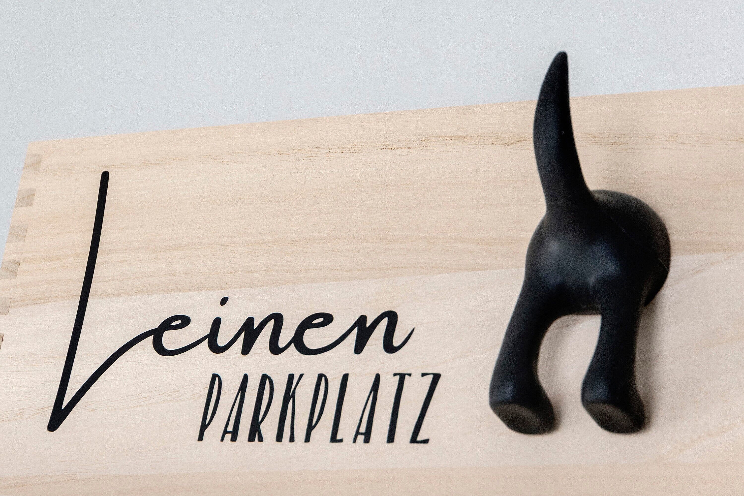 Un segnale di legno con la scritta 'Leinen Parkplatz' e una statuina di un gatto nero.