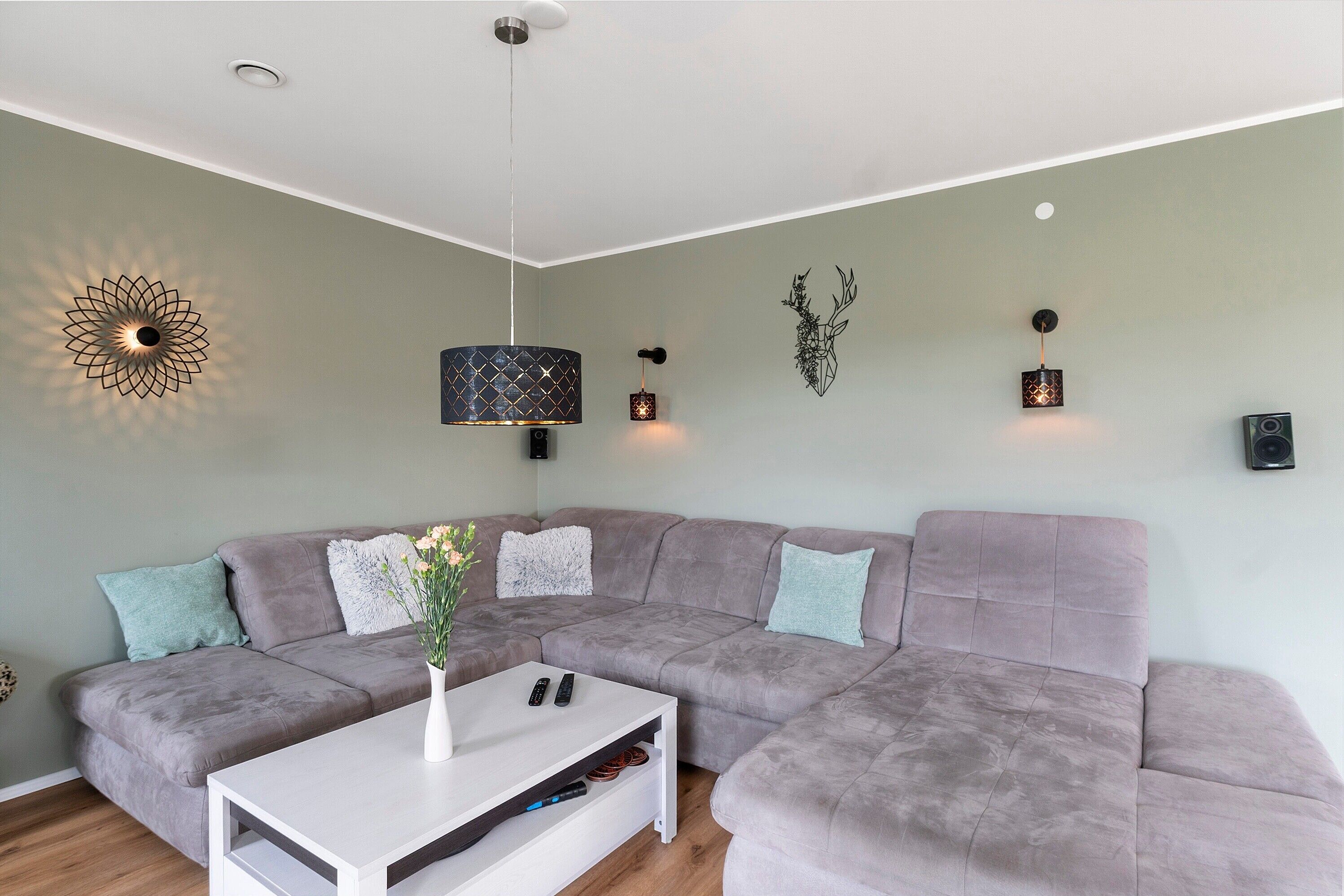 Ein modernes Wohnzimmer mit Ecksofa, einem weißen Couchtisch und dekorativer Wandbeleuchtung.